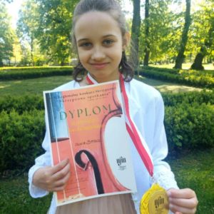 Uczennica z dyplomem i medalem. W tle zieleń parku.