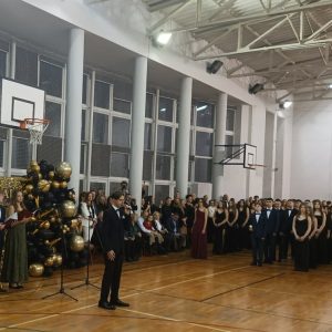 Chłopka trzyma mikrofon w oddali ósmoklasiści ustawieni w rzędach