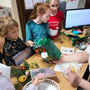 Przy biurku bibliotekarza wesołe dzieci wykonują zadania z kalendarza i losują nagrody.