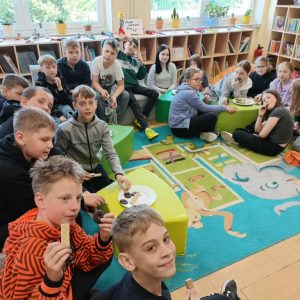Kl. IVA, która najwięcej pomogła w metamorfozie biblioteki. Uśmiechnięci uczniowie siedzą w półokręgu i jedzą ciastka.