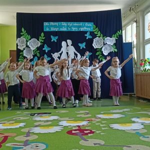 Dziewczynki i chłopcy tańczą na tle dekoracji o rodzinie.