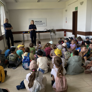 Dzieci siedzą na podłodze, odwrócone do dwóch policjantek przed nimi