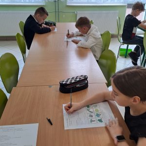 Dzieci, które siedzą przy ławkach i piszą test o lesie.