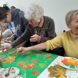 uczestnicy warsztatów malują liśćmi i śmieją się.