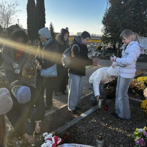 uczniowie i nauczycielki zbierają wypalone znicze przy grobie żołnierzy