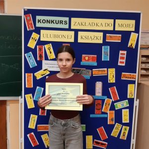 laureatka 1 miejsca prezentuje dyplom na tle tablicy z pracami