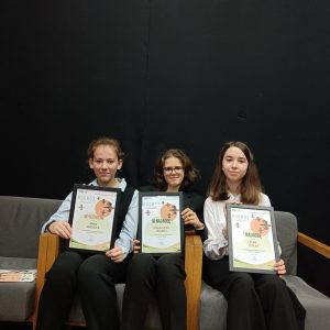 laureatki siedzą na fotelach i pokazują dyplomy.