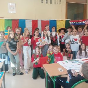 Uśmiechnięta grupa uczniów w barwnych strojach uczestniczących w wydarzeniu, trzymają flagi i plakaty