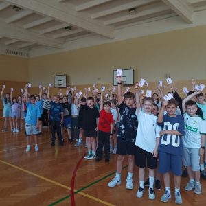 Uśmiechnięte dzieci, w podniesionej ręce, trzymają kartę rowerową.