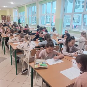grupa uczniów reprezentujących klasy 2 i 3, piszących test na stołówce szkolnej.