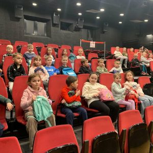 Dzieci z grupy 0 B z uśmiechem siedzą w sali kinowej i oglądają bajkę