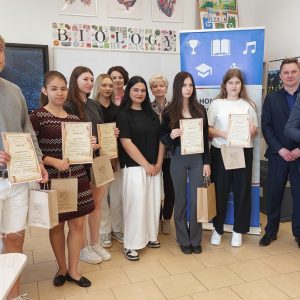 chłopcy i dziewczęta ubrani kolorowo, z prawej strony stoi mężczyzna w okularach ubrany w garnitur