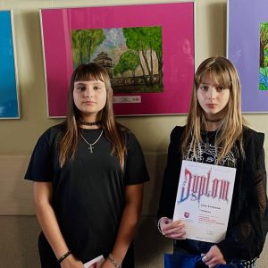 ubrane na czarno laureatki konkursu plastycznego. Jedna z nich trzyma w ręce dyplom