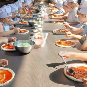 dzieci rozsmarowujący sos na spodzie pizzy