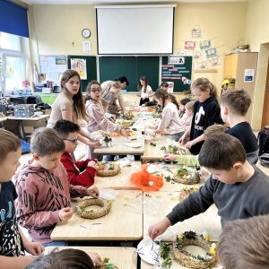 Uczniowie siedzą przy stole i wykonują wielkanocne ozdoby.