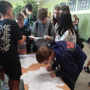Zamyśleni uczniowie rozwiązują łamigłówki, quizy i zagadki matematyczne w przygotowanym kąciku na korytarzu szkoły.