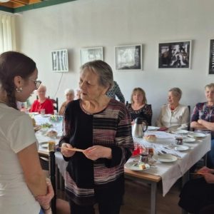 spotkanie wielkanocne z Klubem 50 PLUS: seniorka odbiera życzenia od wolontariuszki