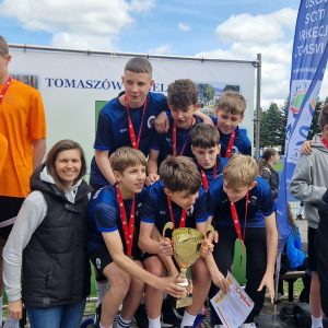 Grupa uczniów z medalami stoi na podium, trzymając puchar i dyplom.