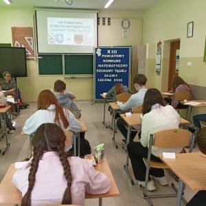 Uczniowie siedzący w ławkach rozwiązujący zadania konkursowe