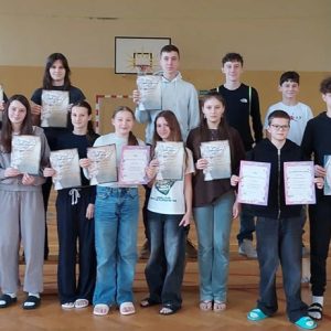 grupa uczniów stojąca w szkolnej sali gimnastycznej, dumnie trzymająca dyplomy.