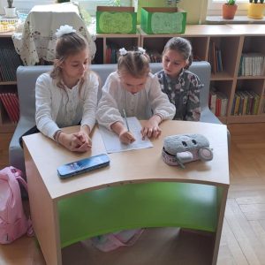 trzy dziewczynki siedzące przy stoliku i rozwiązujące test